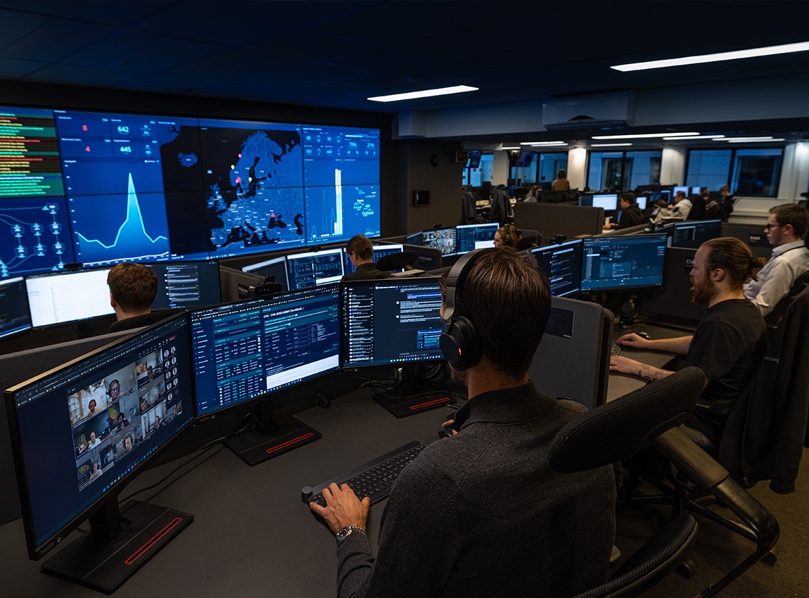 People working in an Operations Center with multiple monitors and large data screens displaying analytics and maps.